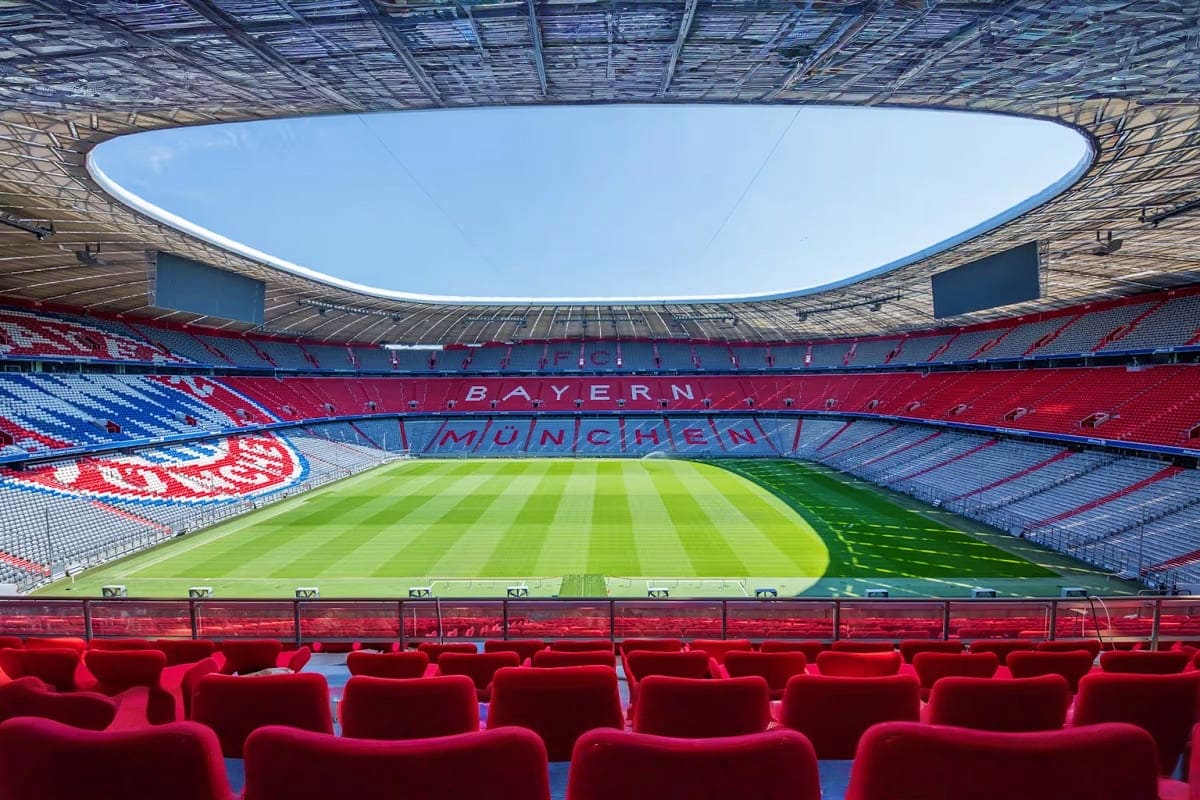 Allianz Arena stadium interior showing red seats, striped pitch, and Bayern Munich branding with open roof design