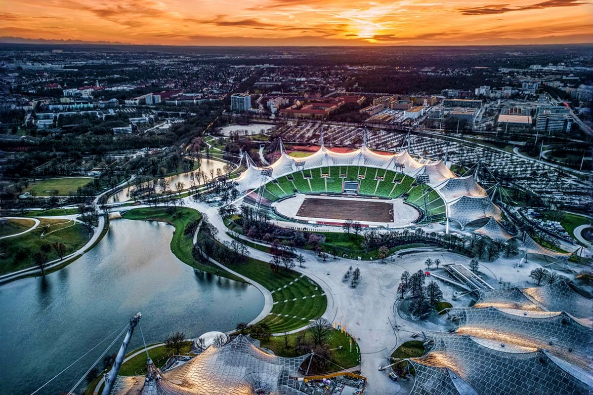 Allianz Arena Behind The Scenes Experience With FC Bayern Museum Visit & Bus Tour Aerial view of Olympic Stadium in Munich at sunset with surrounding park, river, and city landscape in background