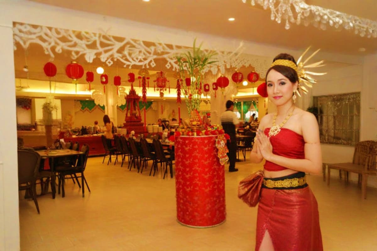 Siam Niramit Show Woman in traditional Thai red silk dress posing in decorated banquet hall with red lanterns and gold accents at Siam Niramit