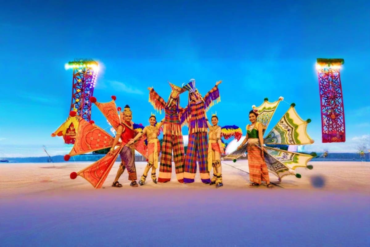 Siam Niramit Show Performers in colorful traditional Thai costumes posing on beach with illuminated theatrical props and structures against blu
