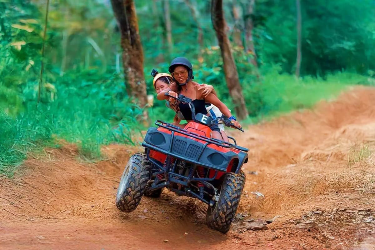 Two people riding a red ATV on a dirt forest trail in Phuket, wearing helmets and safety gear