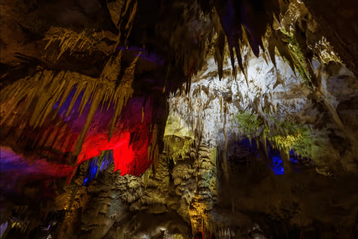Illuminated cave interior with dramatic red and blue lighting on stalactites and stalagmites in Prometheus Cave