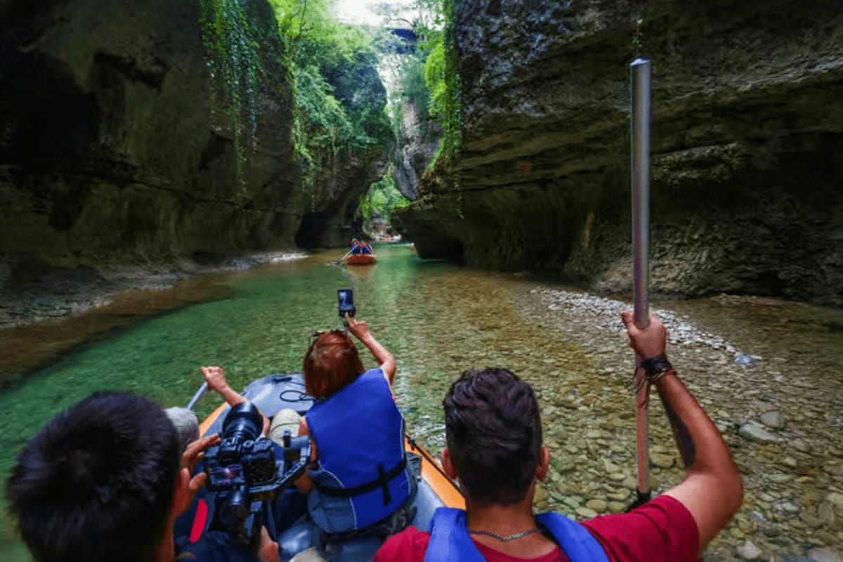 Tourists in blue life jackets kayaking through narrow moss-covered stone canyon with emerald water and towering rock walls
