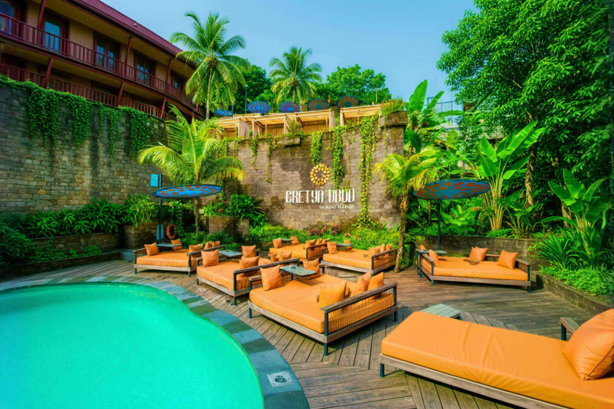 Tropical resort pool courtyard with turquoise swimming pool, orange loungers, stone walls, and lush palm trees and vegetation