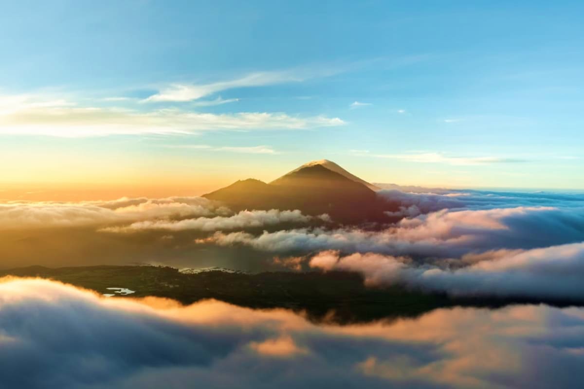 Mount Batur volcano at sunrise surrounded by clouds and mist during early morning light