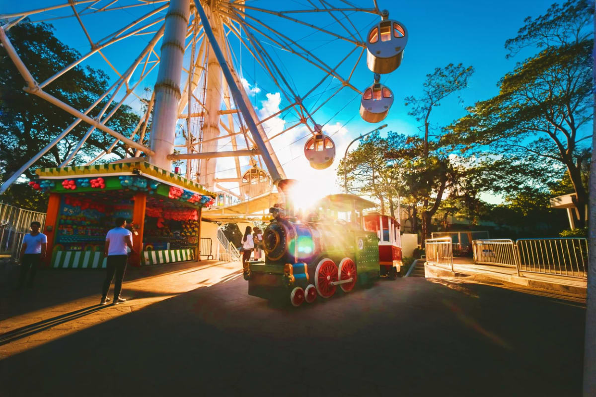 Ferris wheel and colorful train ride at Sky Ranch amusement park with sunny blue sky and trees