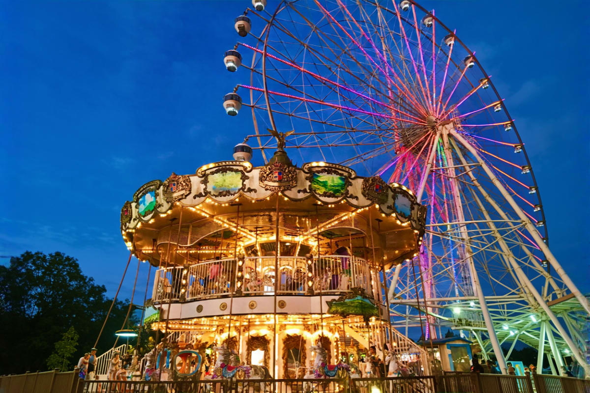 Illuminated carousel swing ride with Ferris wheel lit in purple against blue evening sky at amusement park