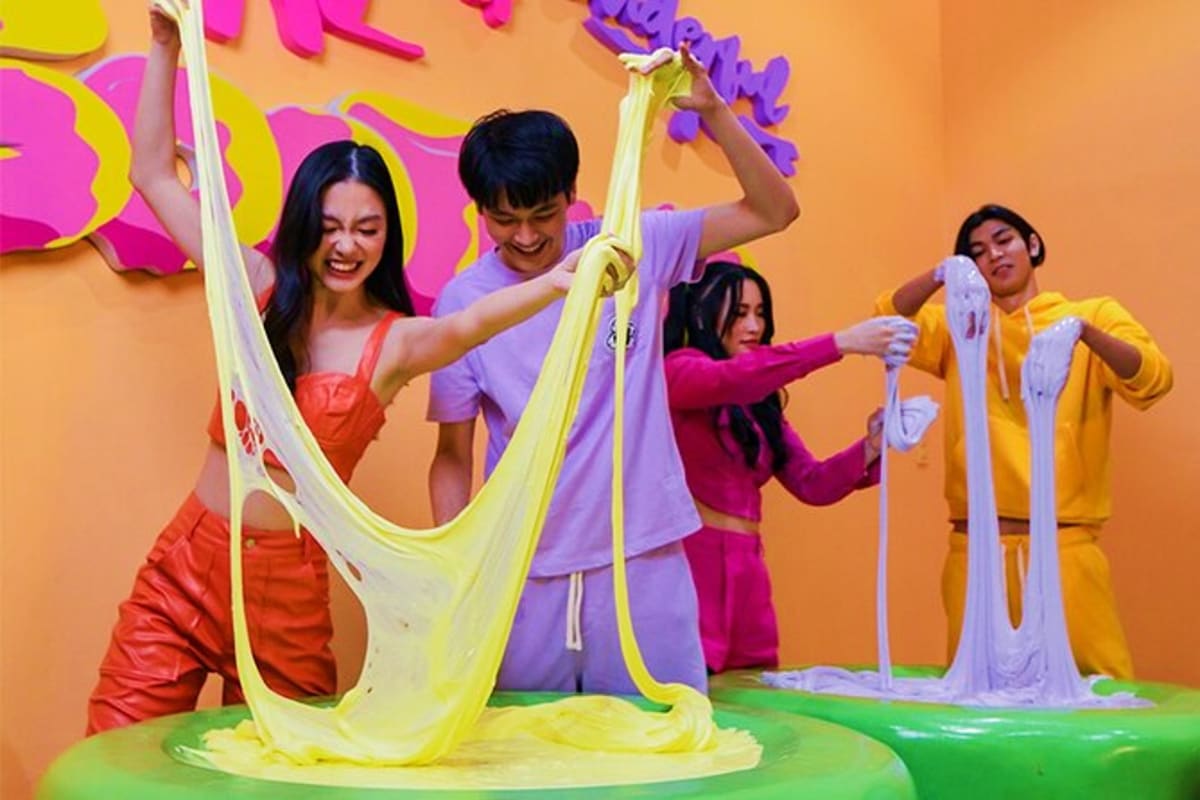 Group of young adults playing with stretchy yellow slime at colorful interactive exhibit in Gootopia indoor activity center