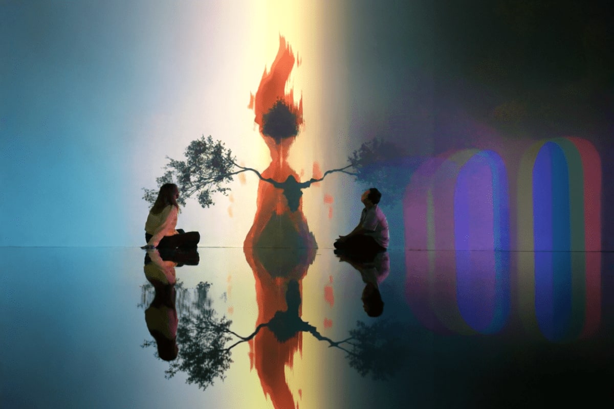 Art In Island The Media Square Silhouette artwork display at Art In Island showing two visitors observing illuminated fire and tree figure with colorful lig