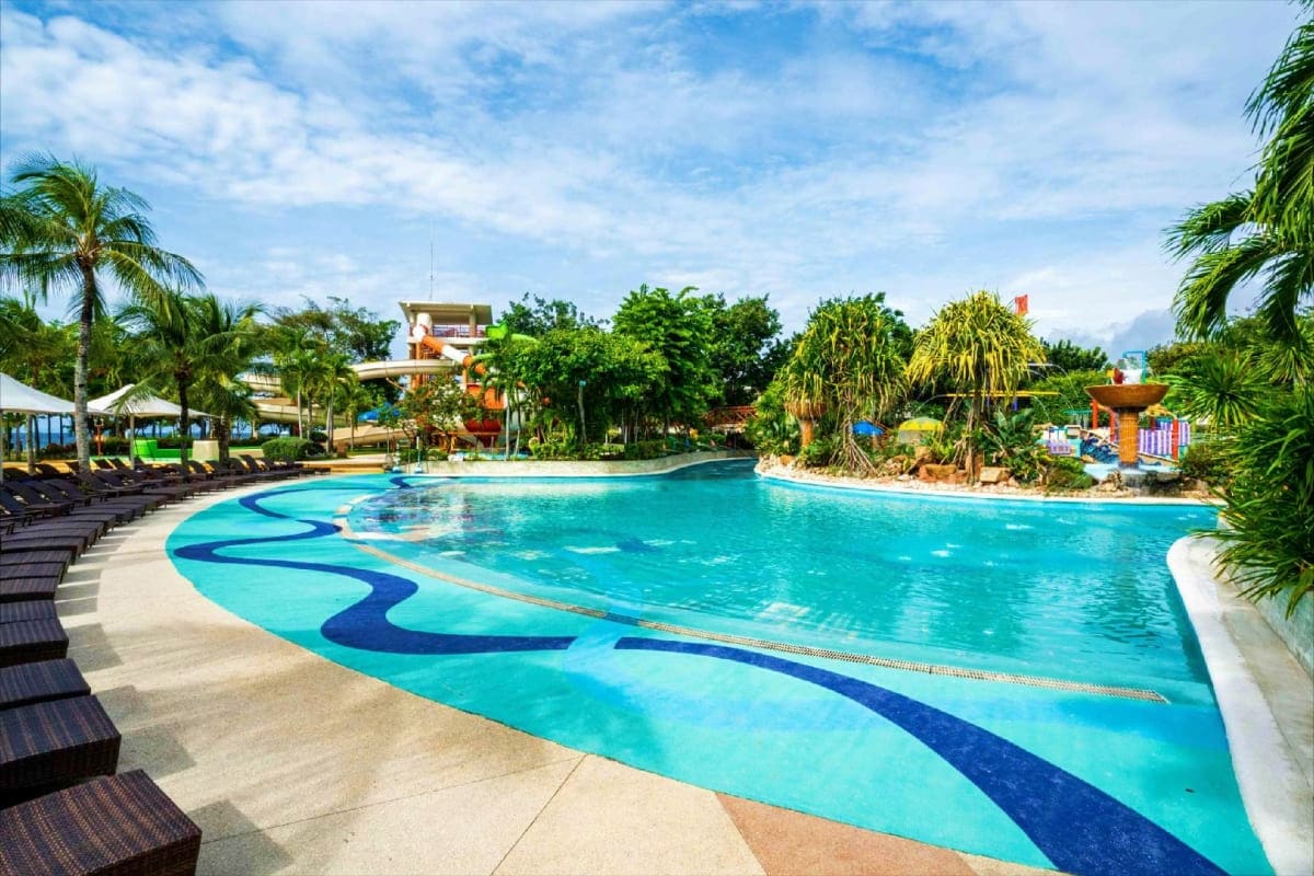 Large turquoise swimming pool with wave pattern design at Jpark Island Resort, surrounded by palm trees and lounge chairs