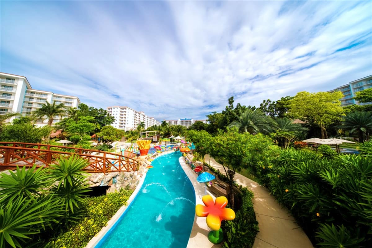 Lazy river with turquoise water winding through tropical gardens at Jpark Island Resort, with apartment buildings and blue sk