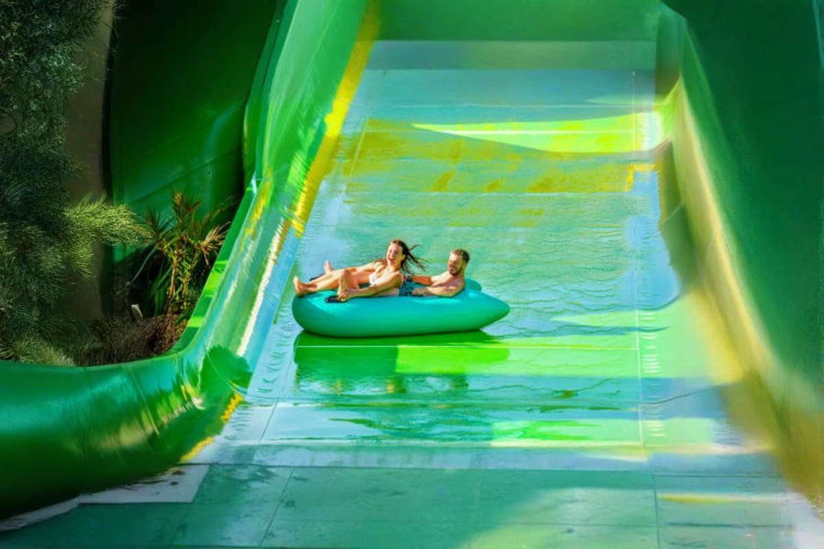 Waterbom Bali Two people floating on a teal inflatable raft inside a bright green water slide tunnel at Waterbom Bali water park