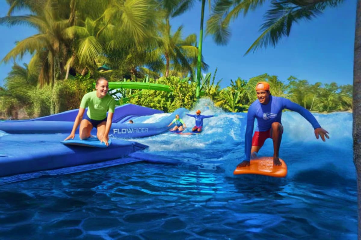 Waterbom Bali Waterbom Bali water park with visitors surfing on wave pool, blue inflatables, and palm trees under clear sky