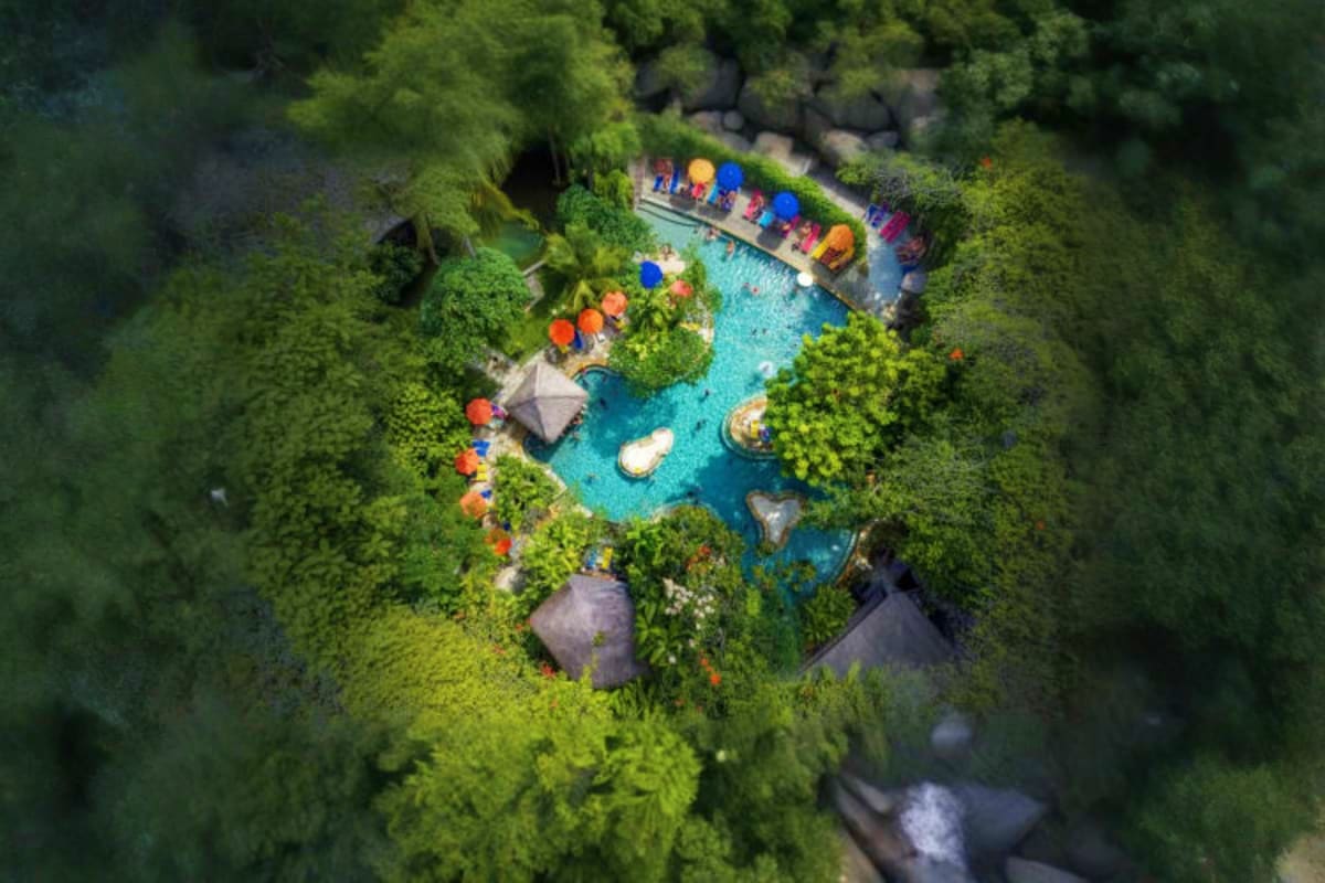 Waterbom Bali Aerial view of Waterbom Bali water park surrounded by lush tropical forest with turquoise pools, colorful umbrellas, and loun