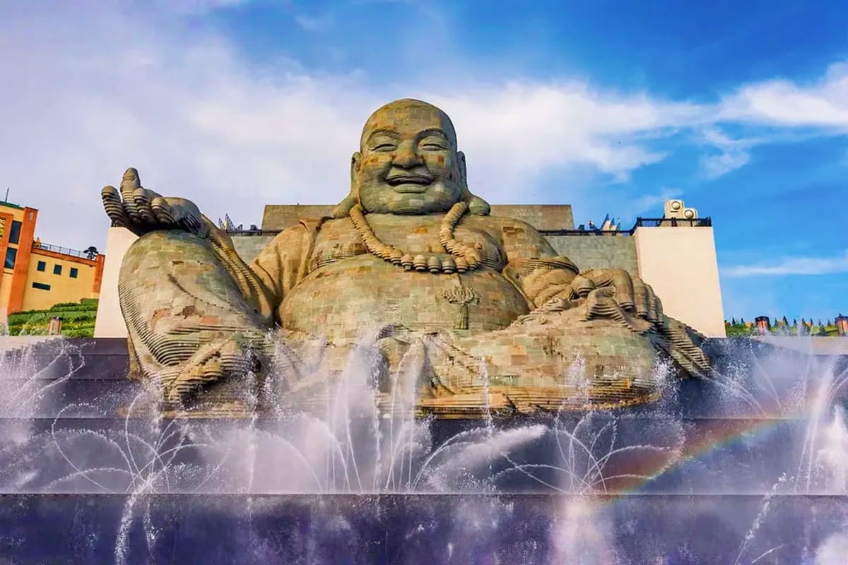 Large smiling Buddha statue with fountains spraying water in foreground at Sun World Ba Den tourist attraction