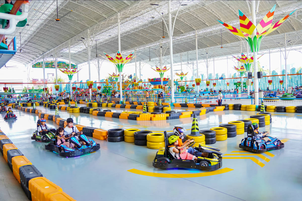 Indoor go-kart racing track at Suoi Tien Theme Park with colorful flower decorations hanging from ceiling and yellow-black ti