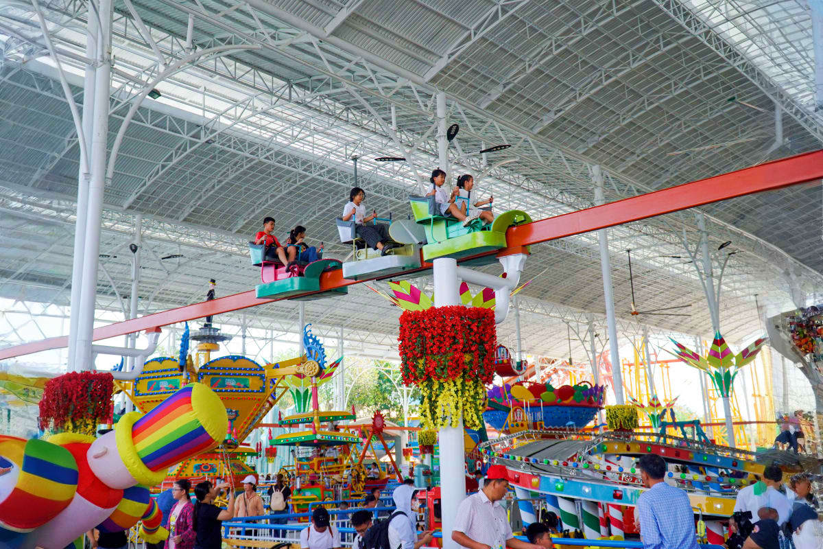 Children riding a colorful airplane ride in a large covered amusement park with hanging flowers and colorful attractions at S