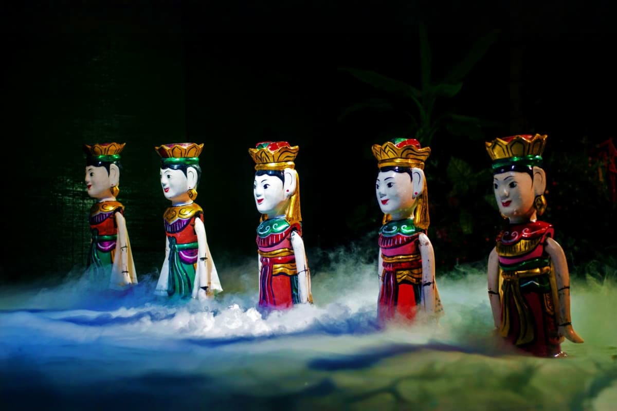 Five illuminated traditional Vietnamese water puppet figures in colorful costumes and golden crowns performing in misty water