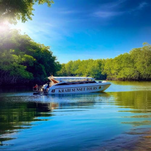 Tour boat named Krabi Sunset Tours on calm turquoise water surrounded by dense green mangrove forests under clear blue sky