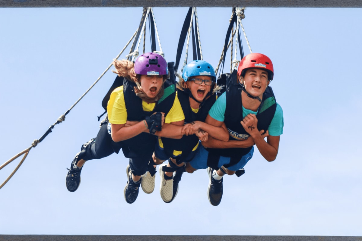 AJ Hackett Sentosa Three people ziplining at AJ Hackett Sentosa, suspended in air wearing safety helmets against clear blue sky