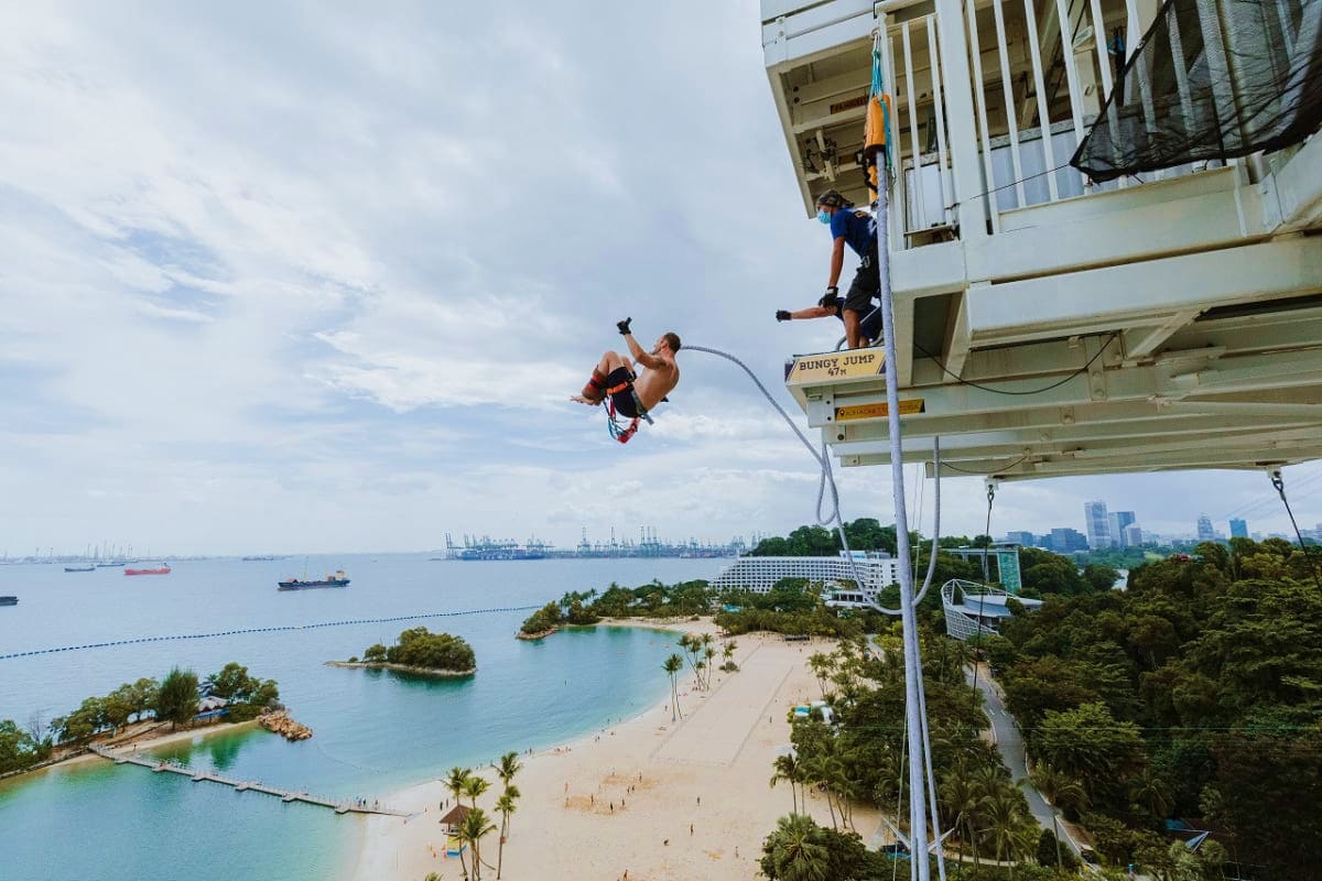AJ Hackett Sentosa Two people bungee jumping from a platform at AJ Hackett Sentosa with beach and coastal cityscape below