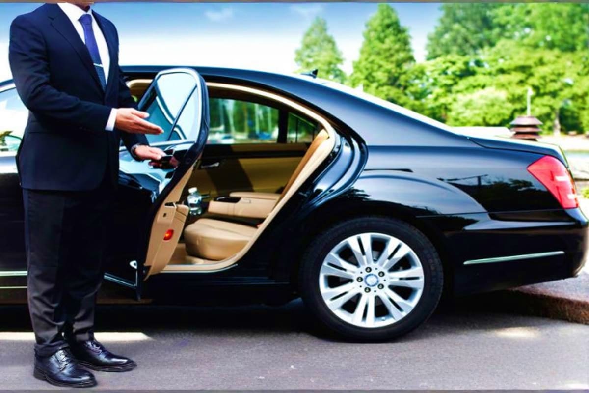 Professional chauffeur in dark suit standing beside black luxury car with open door at airport pickup service