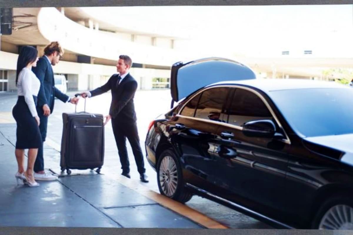 Business travelers with luggage meeting chauffeur next to black luxury car at airport pickup location