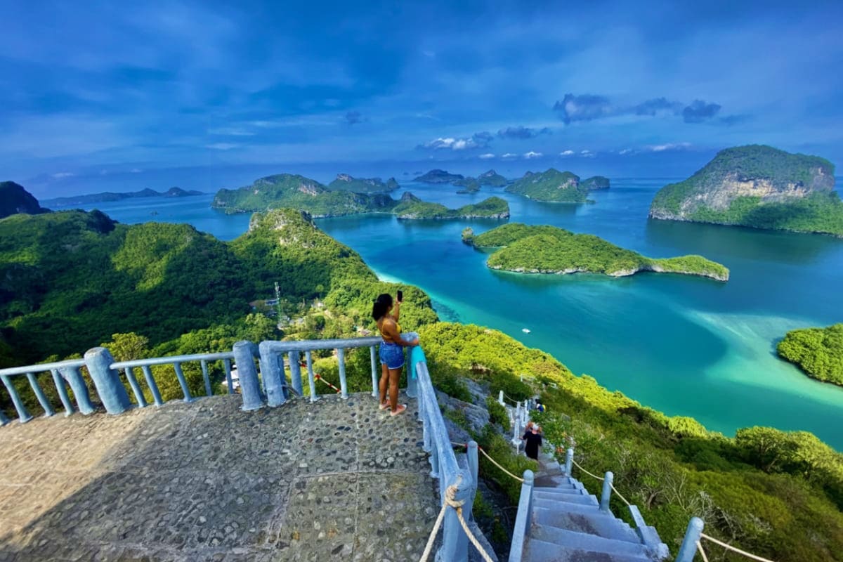 Tourist viewing turquoise waters and lush green islands from elevated viewpoint with white railings at Angthong National Mari