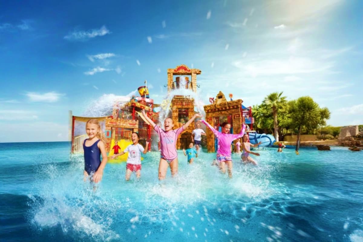 Children playing in turquoise water in front of a large golden temple-themed water park structure with water slides and attra