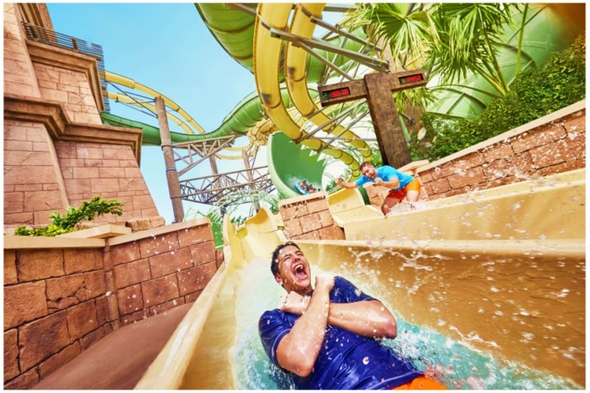 Man riding yellow water slide at Atlantis Aquaventure Waterpark with splash and tropical surroundings