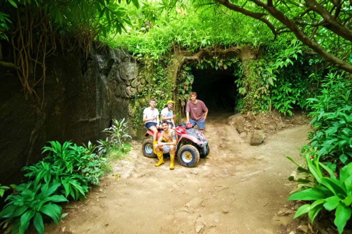 Bali ATV Tour Group of tourists on ATV quad bike in lush jungle tunnel with verdant vegetation and stone archway in Bali