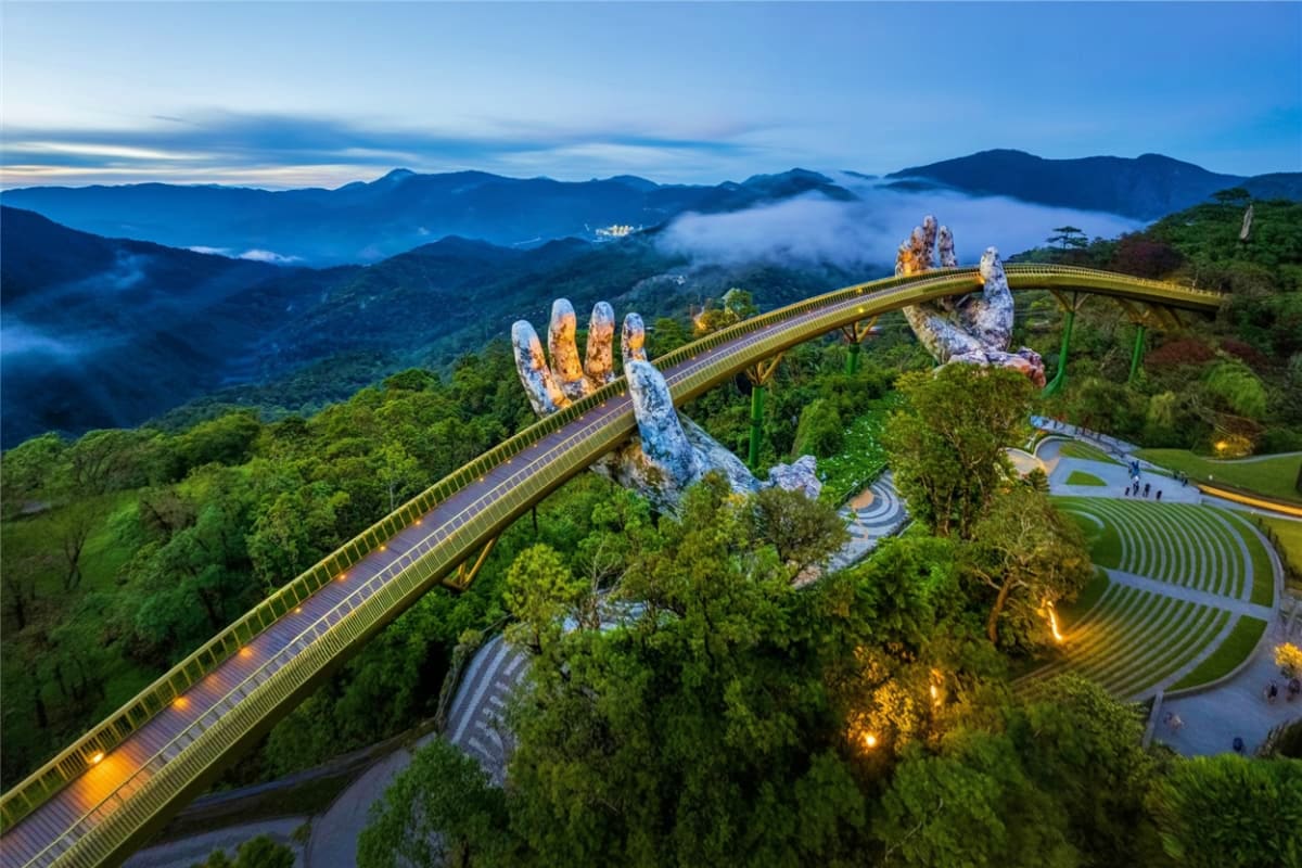 Golden Bridge with giant stone hands at Ba Na Hills, Vietnam, surrounded by lush green mountains and mist at dusk