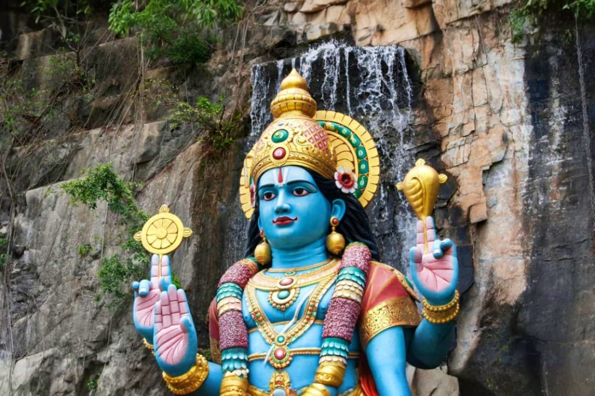 Colorful Hindu deity statue with blue skin and gold ornaments carved into rock face at Batu Caves temple in Malaysia