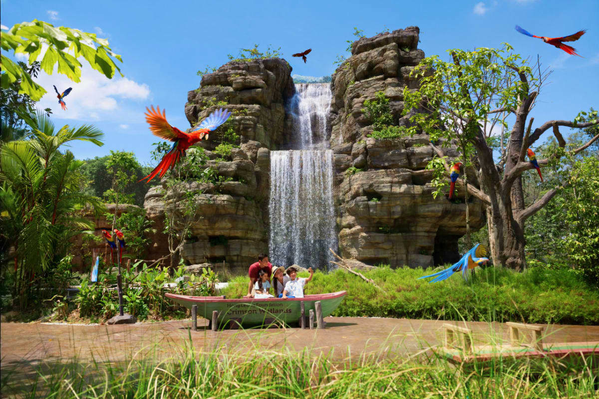 Tropical jungle scene with giant stone heads, waterfall, colorful macaws flying and perched, and visitors in a boat on brown 