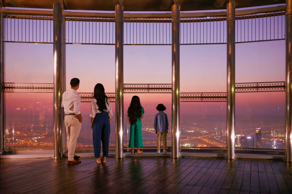Four people viewing cityscape from Burj Khalifa observation deck at dusk with illuminated city lights below