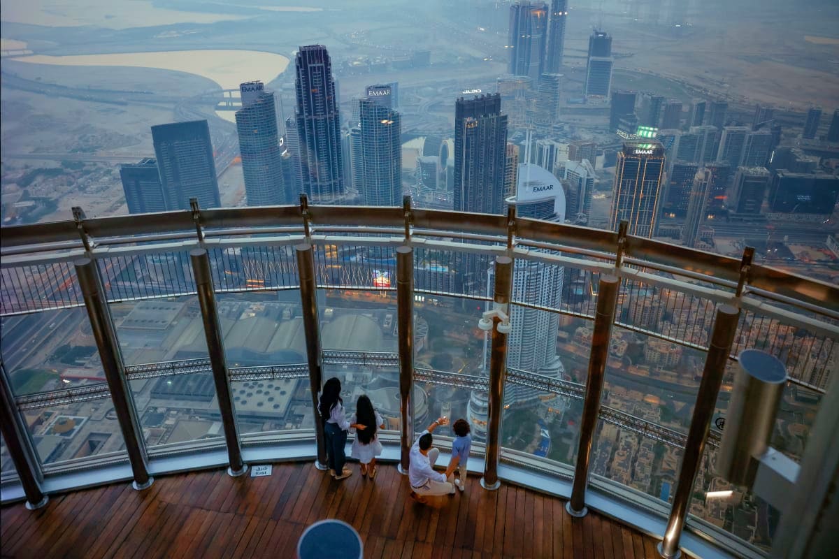 Visitors viewing Dubai skyline and Arabian Gulf from Burj Khalifa observation deck with floor-to-ceiling glass panels