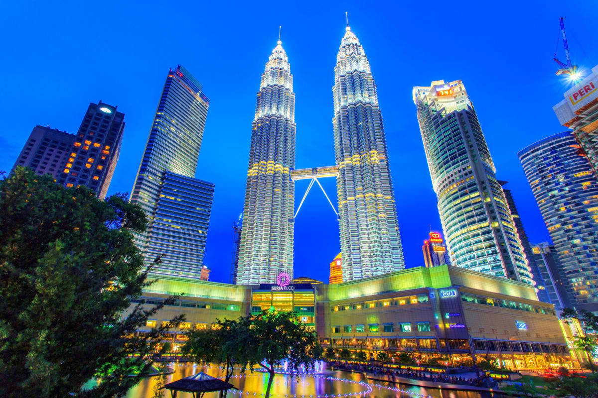 Petronas Twin Towers illuminated at night in Kuala Lumpur skyline with surrounding skyscrapers and shopping mall below