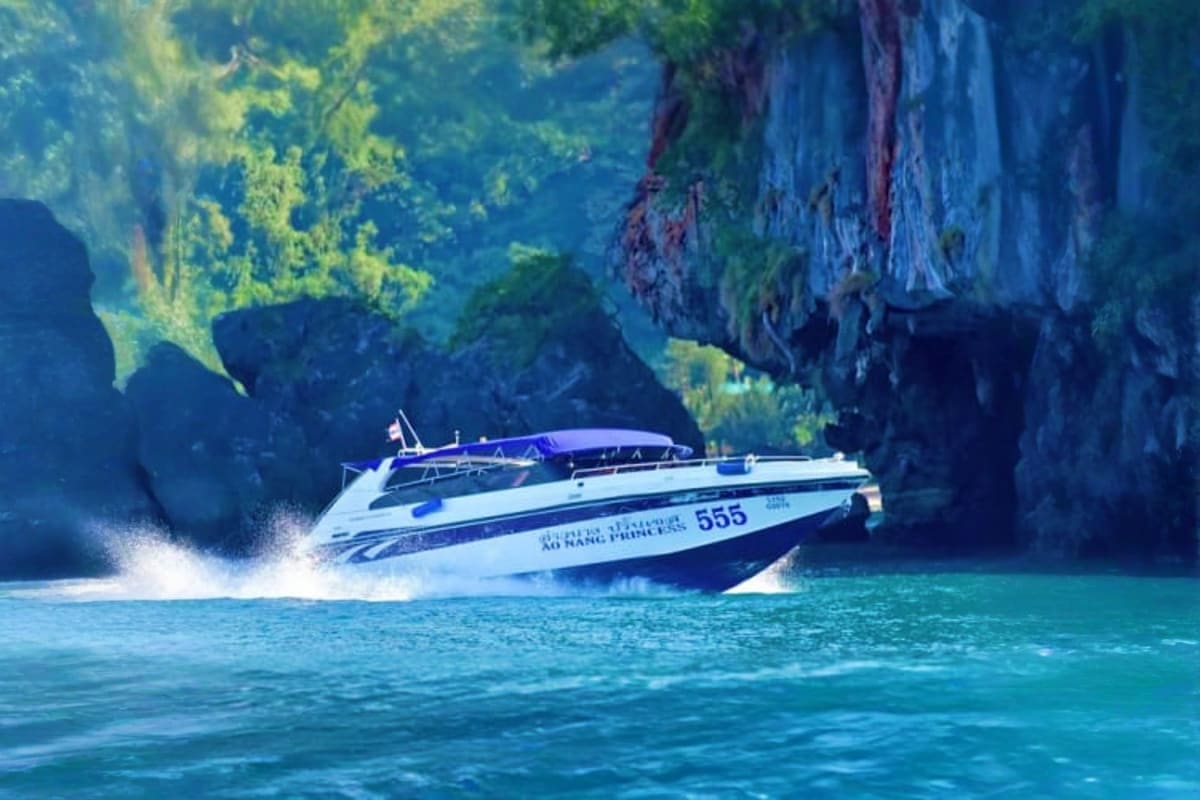 Speed boat with blue canopy traveling past dramatic limestone cliffs in turquoise tropical waters