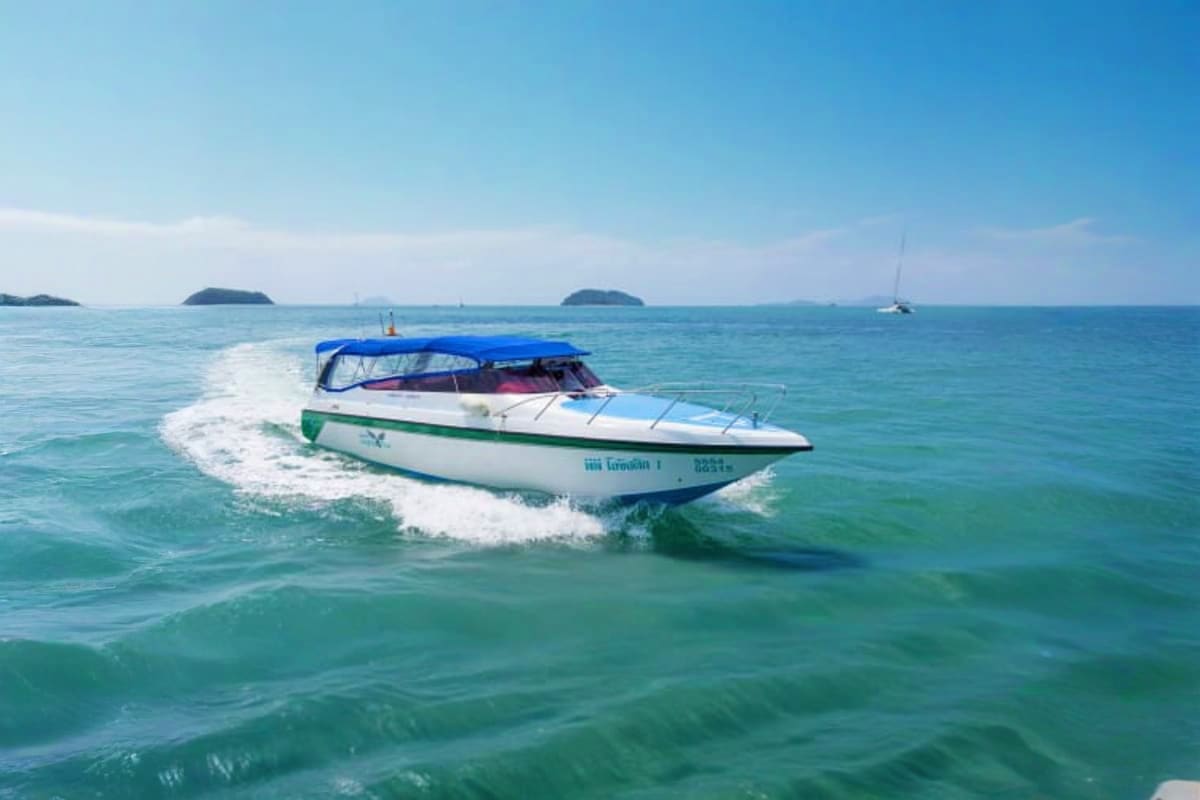 White and green speedboat with blue canopy riding through turquoise waves toward tropical islands under clear sky