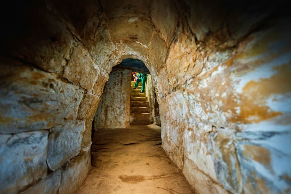 Cu Chi Tunnel Private Transfer Narrow underground tunnel with stone walls and wooden stairs leading upward toward daylight at Cu Chi Tunnels