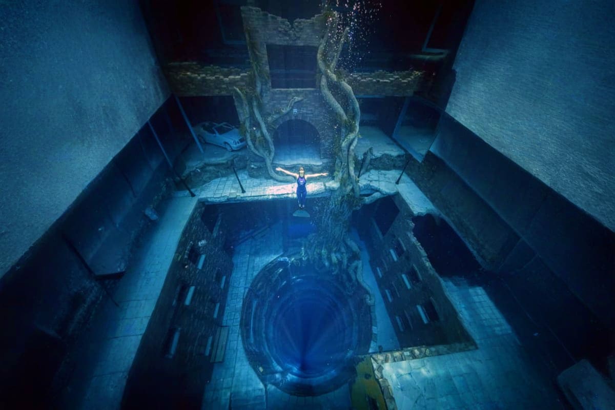 Deep Dive Dubai Diver standing on platform inside submerged sunken city at Deep Dive Dubai underwater attraction
