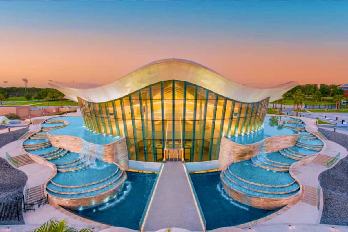Deep Dive Dubai Modern aquatic facility at sunset with illuminated wavy roof structure and symmetrical pools with curved steps on either side