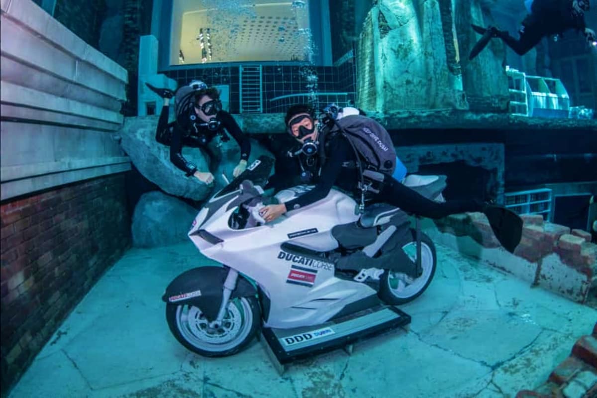 Deep Dive Dubai Two scuba divers on a white Ducati motorcycle inside an underwater submerged structure at Deep Dive Dubai