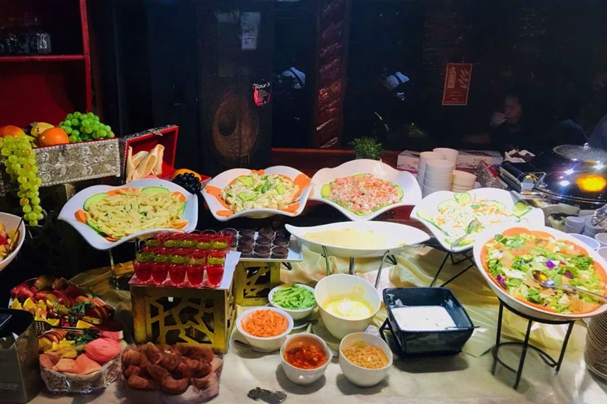 Buffet spread of Asian cuisine dishes including noodles, rice, seafood, and fresh vegetables displayed on white plates during