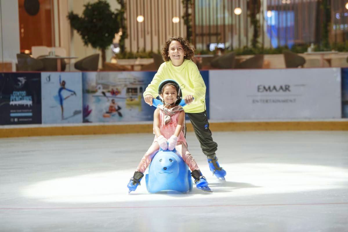 Dubai Ice Rink Two children ice skating at Dubai Ice Rink, one holding a blue penguin-shaped skating aid, with modern rink facility and deco