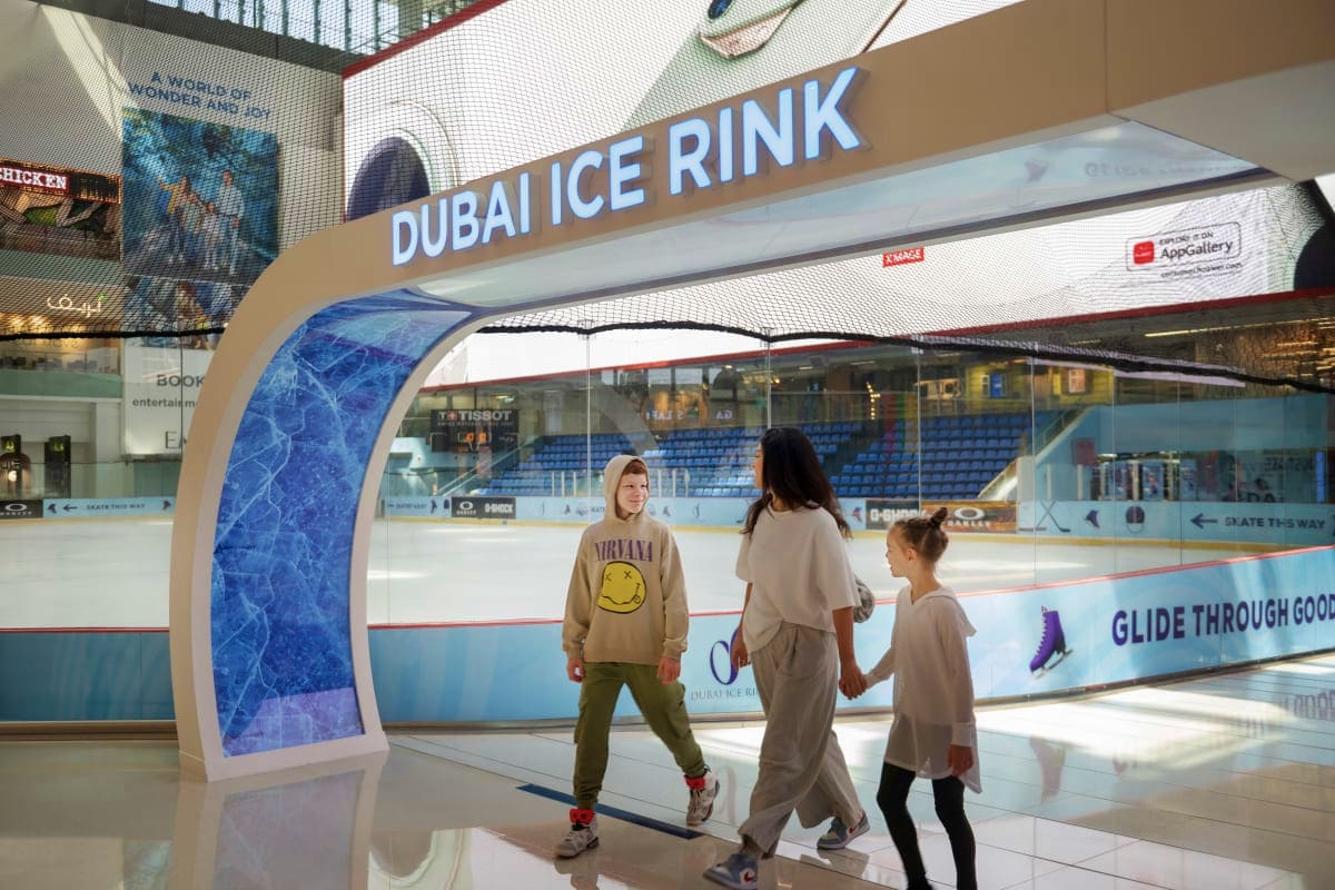Dubai Ice Rink Mother and two children walking past the illuminated Dubai Ice Rink entrance sign in a shopping mall, with ice rink visible t