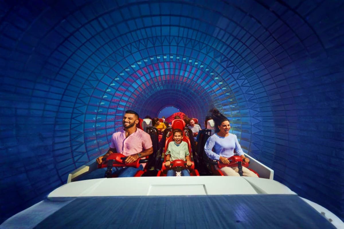 Ferrari Theme Park Abu Dhabi Family riding red roller coaster through blue illuminated tunnel at Ferrari Theme Park Abu Dhabi