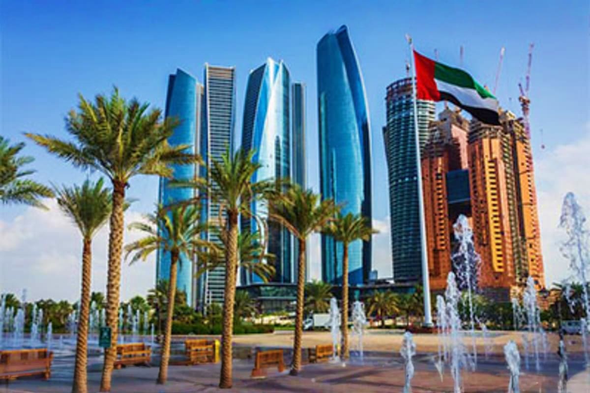 Abu Dhabi skyline with modern blue skyscrapers, palm trees, UAE flag, and waterfront fountains