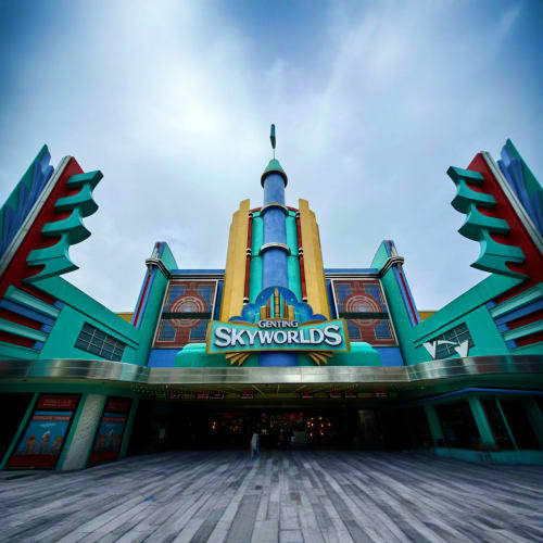 Skyworlds theme park entrance with turquoise art deco architecture and central rocket tower under cloudy sky