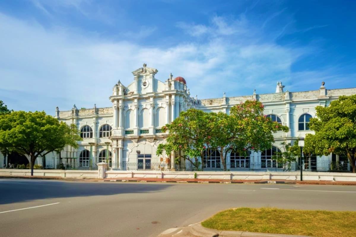 Colonial-era white building with red dome roof and ornate architecture surrounded by green trees in Penang city center